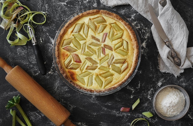 Pastel de ruibarbo casero en una mesa oscura con ingredientes y un primer plano plano