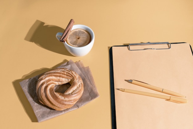 Pastel, taza de té o vino caliente y hoja de currículum en el fondo de color champán zarpada, vista superior.