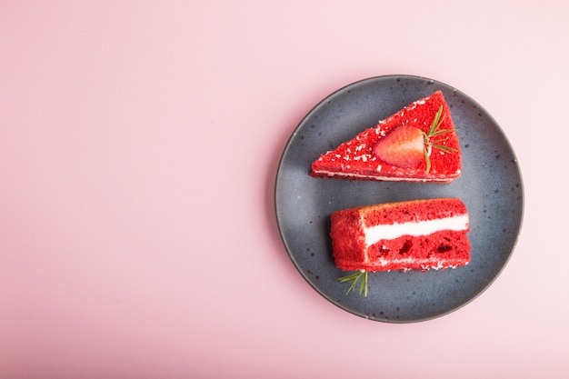 Pastel de terciopelo rojo casero con crema de leche y fresa en placa de cerámica azul aislado en un fondo rosa pastel. Vista superior, espacio de copia.