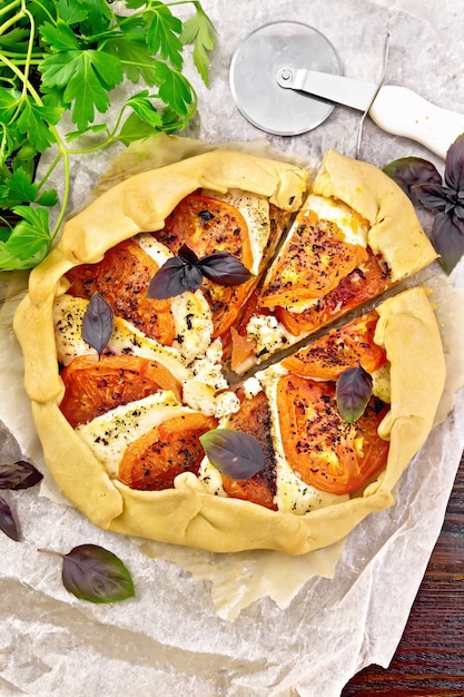 Pastel con tomates, requesón y albahaca morada sobre pergamino, perejil sobre una tabla de madera de fondo desde arriba