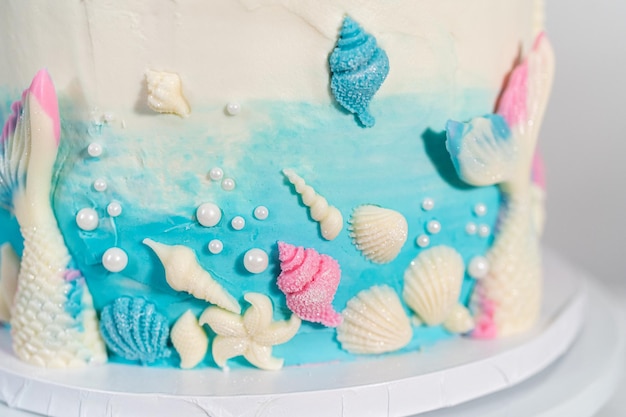 Pastel de vainilla de 3 capas con temática de sirena decorado con colas de sirena de chocolate y conchas marinas en un soporte de pastel blanco.