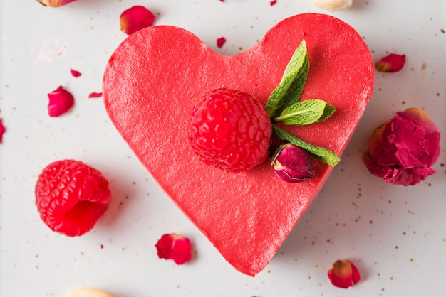 Pastel vegano crudo rojo en forma de corazón con frambuesas frescas, menta y flores secas. Postre del día de San Valentín. vista superior