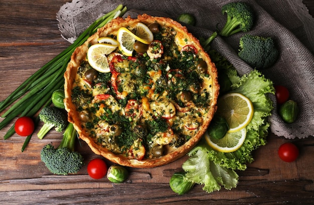 Foto pastel de verduras con brócoli, guisantes, tomates y queso sobre fondo de madera