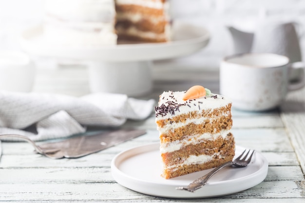 Pastel de zanahoria casero saludable con glaseado de queso crema sobre mesa de madera blanca