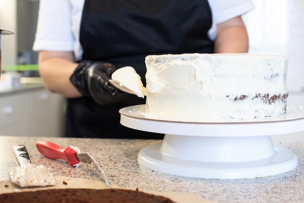 Foto pasteleiro cozinheiro confeiteiro ou padeiro em luvas pretas e avental de cozinha preto faz um bolo. bolo de aniversário feito em casa. conceito de pastelaria caseira, cozinhar bolos, hobby. pequena empresa doméstica feminina.