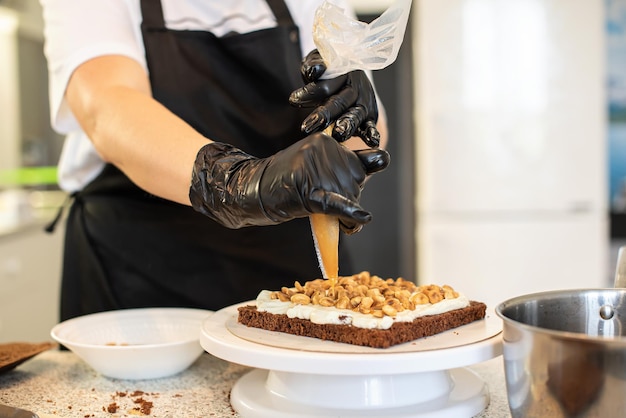 Pasteleiro cozinheiro confeiteiro ou padeiro em luvas pretas e avental de cozinha preto faz um bolo. Bolo de aniversário feito em casa. Conceito de pastelaria caseira, cozinhar bolos, hobby. Pequena empresa doméstica feminina.