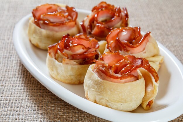 Pastelería casera de masa con jamón en forma de rosa sobre plato blanco