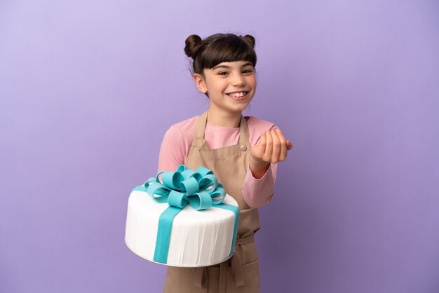 Pastelería niña sosteniendo un gran pastel aislado en la pared púrpura que invita a venir con la mano. Feliz de que hayas venido