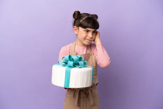 Pastelería niña sosteniendo un gran pastel aislado sobre fondo púrpura frustrado y cubriendo las orejas