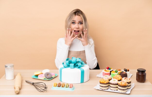 Pastelero adolescente con un gran pastel en una mesa con expresión facial sorpresa