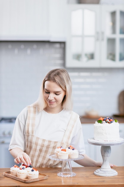 Pastelero confitero joven mujer caucásica decorar pastel en la mesa de la cocina Pasteles cupcakes y postre dulce