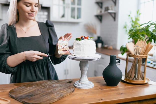 Pastelero confitero joven mujer caucásica con pastel en la mesa de la cocina