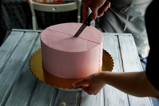 El pastelero cortó el pastel con un cuchillo largo. Cuidado de las manos. Corta un pastel rosa con un estilo minimalista y sin adornos.