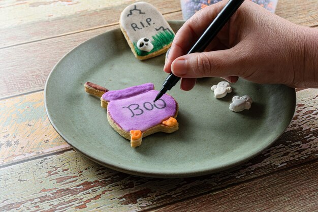 Pastelero escribiendo en una galleta de mantequilla con forma de caldero púrpura (vista frontal).