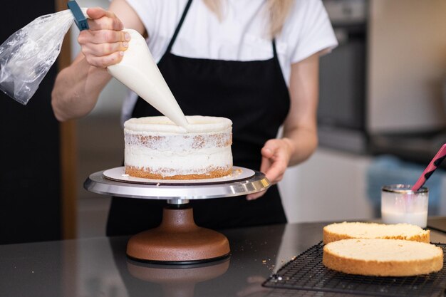 Pastelero experto untando crema blanca alrededor de capas de pastel sin azúcar con cono de pastelería