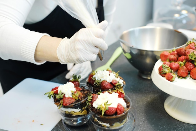 El pastelero exprime la crema de una bolsa de confitería sobre fresas frescas que decoran un postre de chocolate