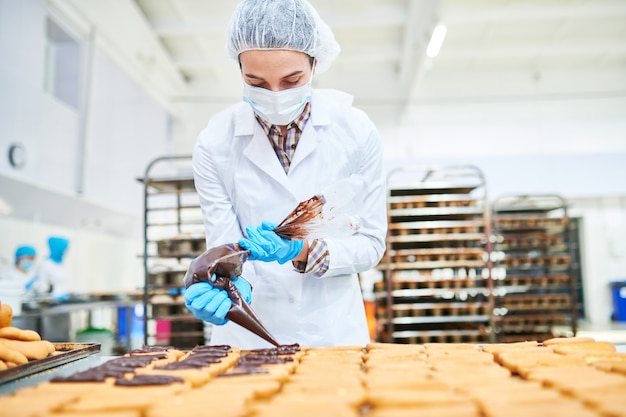 Pastelero exprimiendo crema de chocolate de la bolsa de pastelería