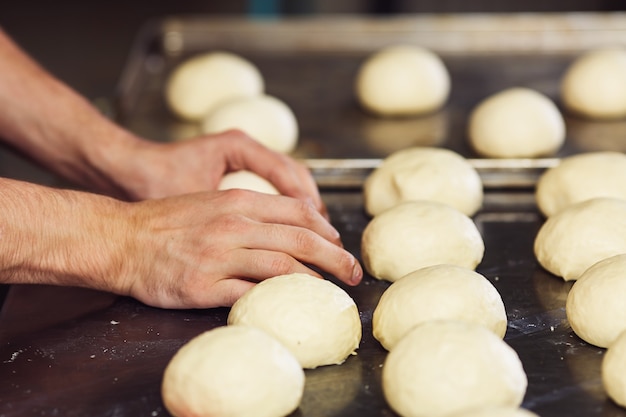 El pastelero forma bollos redondos con la masa y los extiende sobre una bandeja de metal.