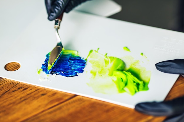 El pastelero con guantes de goma negros revuelve la crema de colores con una espátula para decorar el pastel. colorante alimentario para crema.