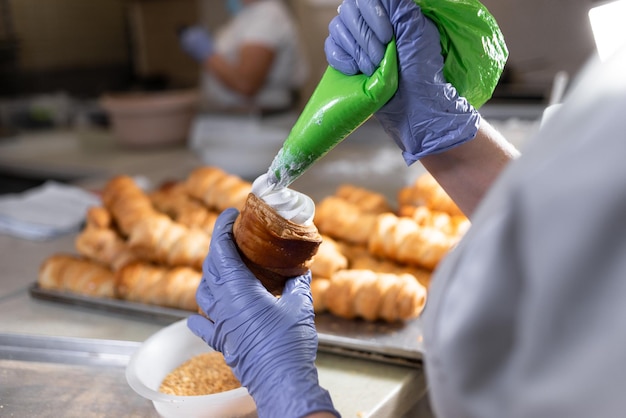 Un pastelero llena un tubo de hojaldre dulce con proteínas batidas de una manga pastelera El proceso de producción en la cocina de la panadería Postres dulces