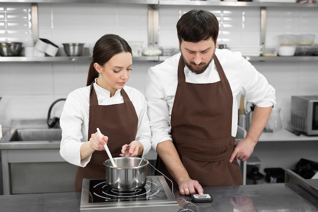 Pasteleros de hombre y mujer preparan el postre juntos en una cocina profesional cocinan jarabe y crema