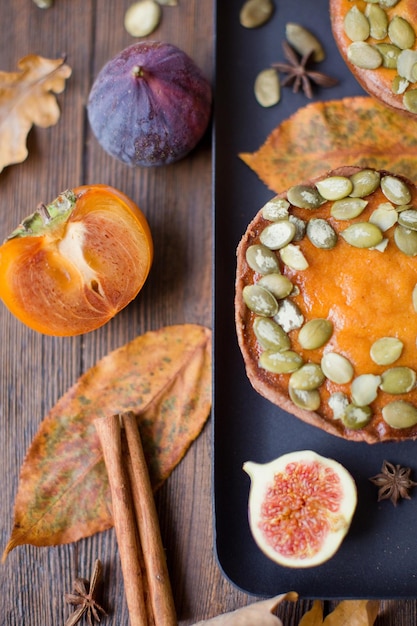 Pasteles de calabaza en un plato negro con higos, palitos de canela, anís estrellado y caquis Concepto de cena de acción de gracias de otoño Sabrosa panadería de otoño