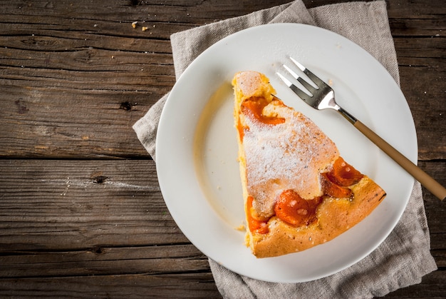 Pasteles caseros de otoño y verano al horno. Bizcocho con albaricoques. Cortar en trozos, plato, tenedor. Sobre la vieja mesa rústica de madera. Copia espacio vista superior