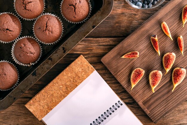 Foto pasteles de chocolate caseros en utensilios para hornear higos frescos y cuaderno sobre fondo de madera plano culinario lay vista superior