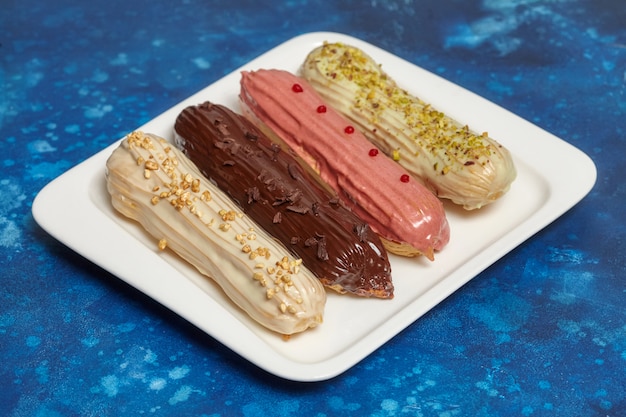 Pasteles de eclair coloridos con crema en la pared azul