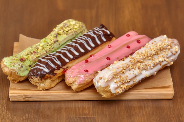 Pasteles de eclair coloridos con crema sobre tabla de madera