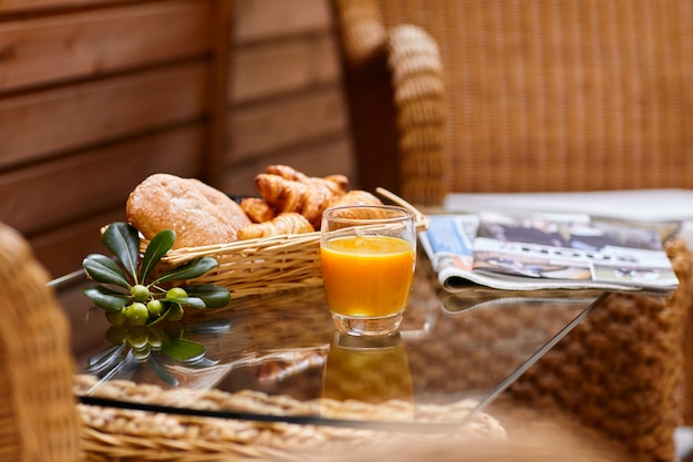 Pasteles frescos, jugo de naranja, rama de olivo y periódico fresco sobre la mesa para el desayuno.