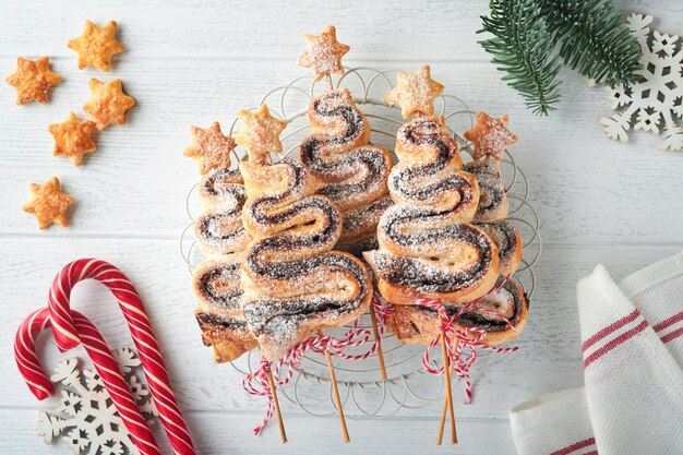 Pasteles de hojaldre con forma de árbol de Navidad con polvo de azúcar relleno de chocolate y piruletas sobre fondo blanco de madera Aperitivo de Año Nuevo de Navidad Idea festiva para la cena de Navidad o Año Nuevo