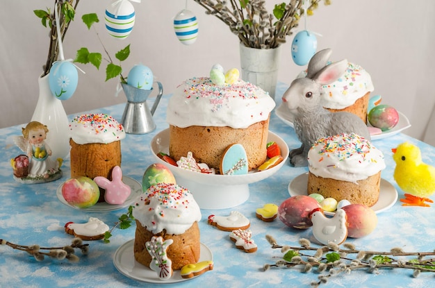 Pasteles y huevos de Pascua en una mesa festiva de Pascua con sauce y una figurilla de un conejo sobre un fondo azul.