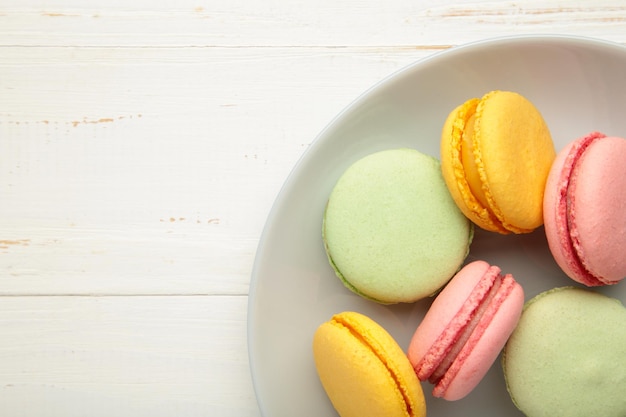 Pasteles de macarons coloridos en plato gris sobre fondo blanco de madera. Pequeños pasteles franceses en un plato.