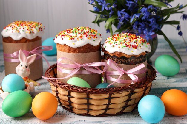 Pasteles de Pascua y huevos coloridos para unas brillantes vacaciones de primavera en una canasta de mimbre sobre un fondo azul.