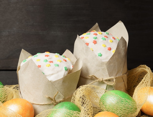 Pasteles de Pascua rodeados de huevos de colores sobre una mesa de madera oscura.