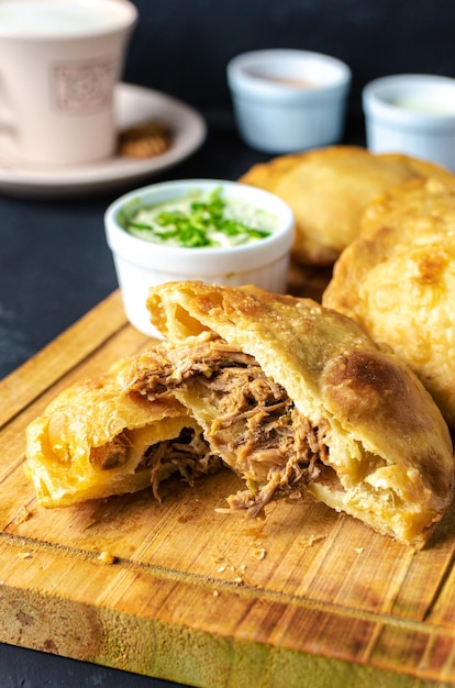 Pastelito tradicional comida venezolana en fondo oscuro, tres salsas y café