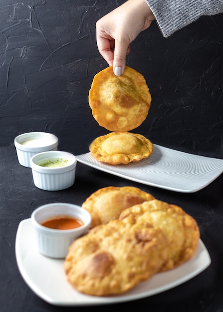 Pastelito tradicional comida venezolana en fondo oscuro, tres salsas