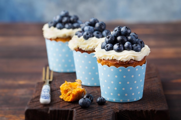 Pastelitos de calabaza decorados con glaseado de queso crema y arándanos frescos sobre un fondo de madera Espacio para copiar