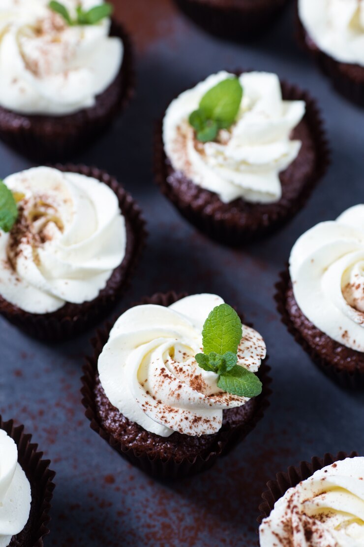 Pastelitos de chocolate decorados con crema de queso y hojas de menta sobre un fondo oscuro