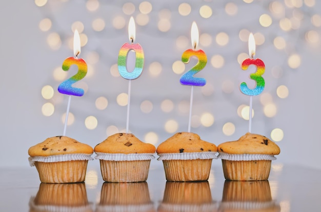 Pastelitos dulces de Navidad y velas en forma de números 2023. Fondo blanco con bokeh. Año Nuevo