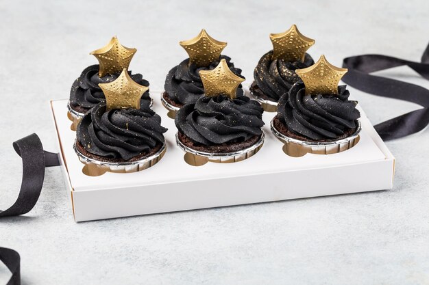 Pastelitos negros decorados con una estrella dorada en una caja sobre un fondo claro