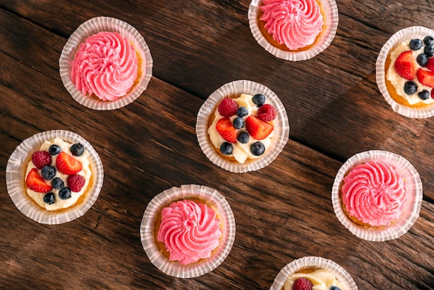 Pastelitos de vainilla planos con bayas frescas en una mesa de madera oscura Cerrar