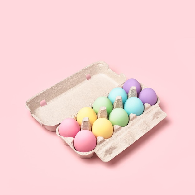 Pastellfarbene Regenbogen-Ostereier im Eierkarton auf rosafarbenem Hintergrund minimal