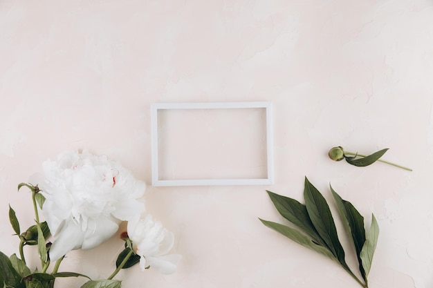 Pastelltisch mit Pfingstrosenblüten und leerem weißen Rahmen mit Kopierraum