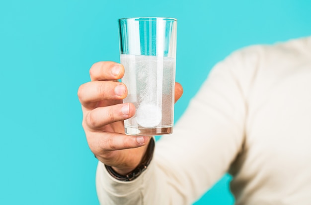 Pastilla blanca y un vaso de agua en manos del hombre.