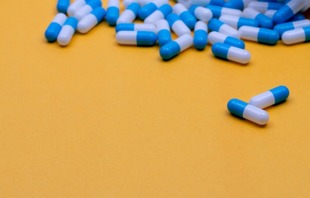 Pastillas de cápsula de antibiótico azul y blanco esparcidas sobre fondo amarillo Resistencia a los antibióticos