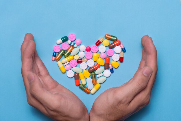 Pastillas de colores en forma de corazón cubiertas con manos sobre fondo azul.