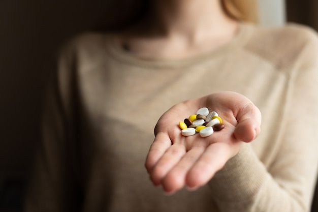 Pastillas de colores y medicamentos en la mano sobre un fondo oscuro