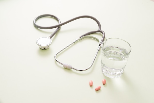 Pastillas de colores y un vaso de agua y un estetoscopio.